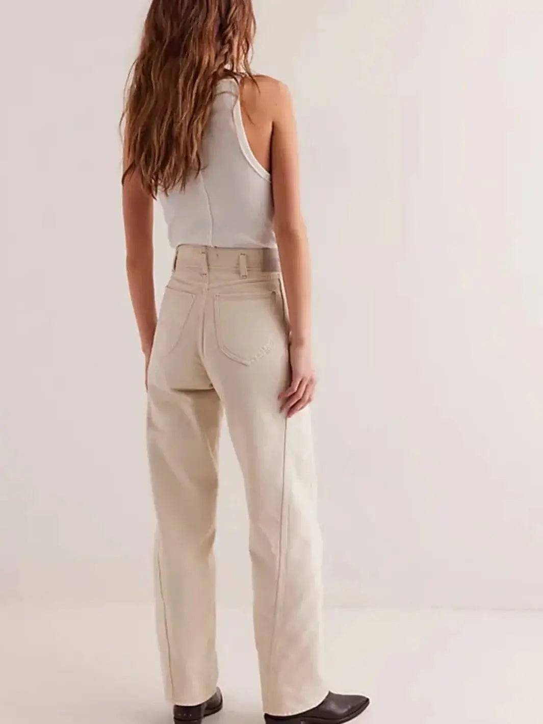 A view from behind shows a model wearing the high-waisted Free People Aster Straight-Leg Jeans - Cream featuring a relaxed straight-leg fit and pointed back pockets styled with dark boots | Twentyseven Toronto