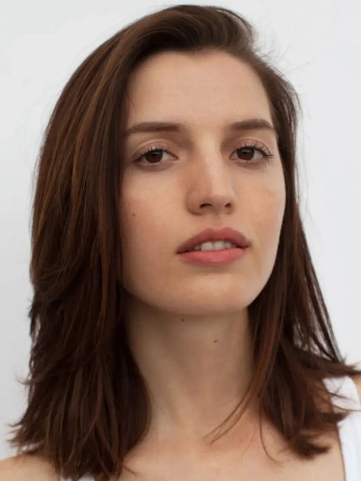 A close-up headshot of a brunette model with smooth, shoulder-length hair styled using R+Co ATLANTIS B5 Moisturizing Shampoo | Twentyseven Toronto