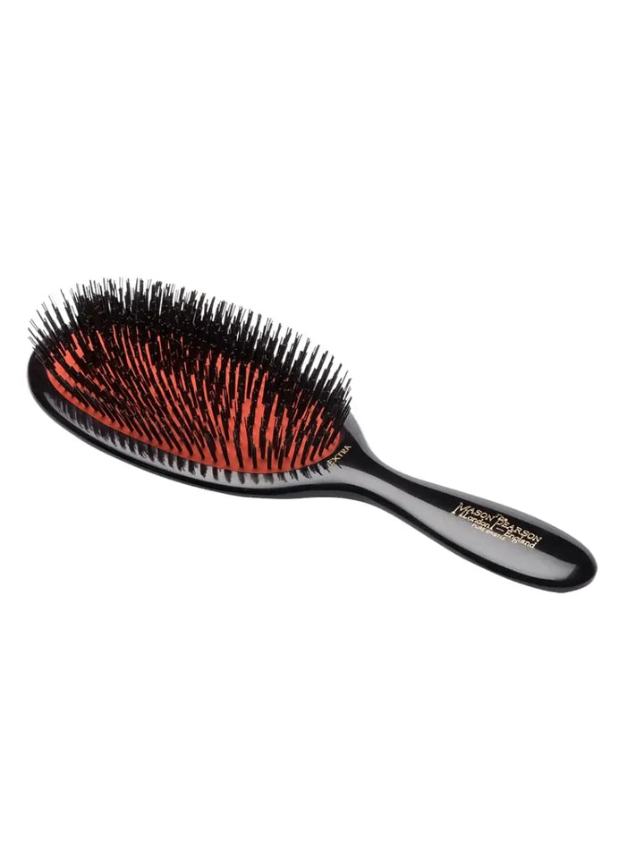 A premium large black hairbrush with natural bristles on a signature red rubber cushion is presented on a clean white background to feature the design of the Mason Pearson Large Extra All Boar Bristle Hairbrush B1 | Twentyseven Toronto