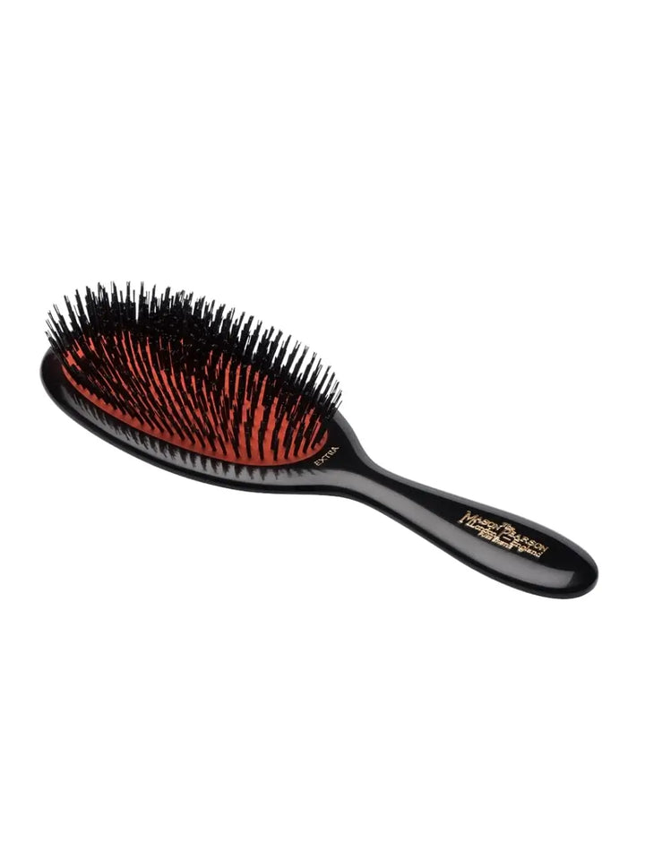 A full-sized black luxury hairbrush with a gold logo on the handle is angled to showcase the dense tufts of a Mason Pearson Small All Extra Boar Bristle Hairbrush B2 | Twentyseven Toronto