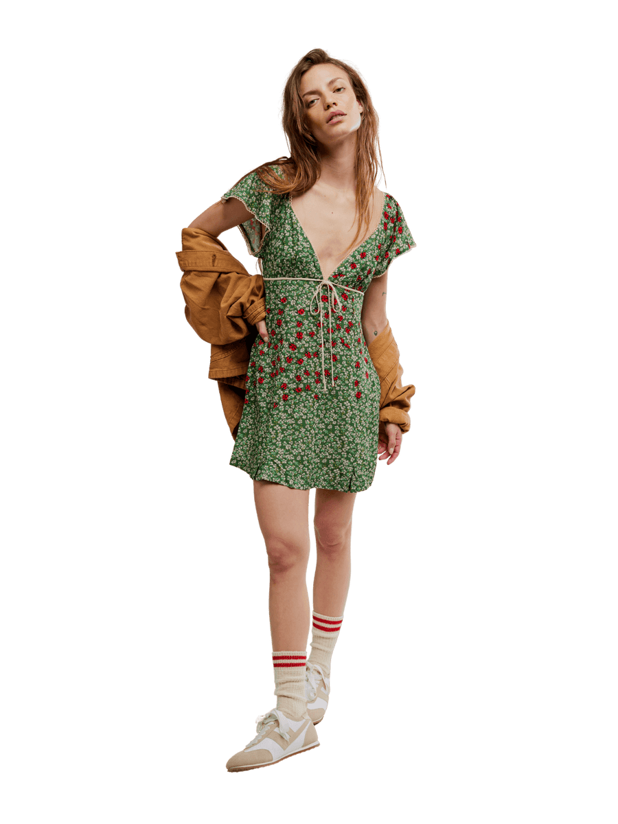Woman wearing a green 'Backroads Mini in Forest Combo' floral dress with a brown jacket from Free People on a transparent background | Twentyseven Toronto
