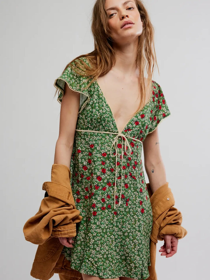Woman wearing a green 'Backroads Mini in Forest Combo' floral dress with a brown jacket from Free People on a white background | Twentyseven Toronto