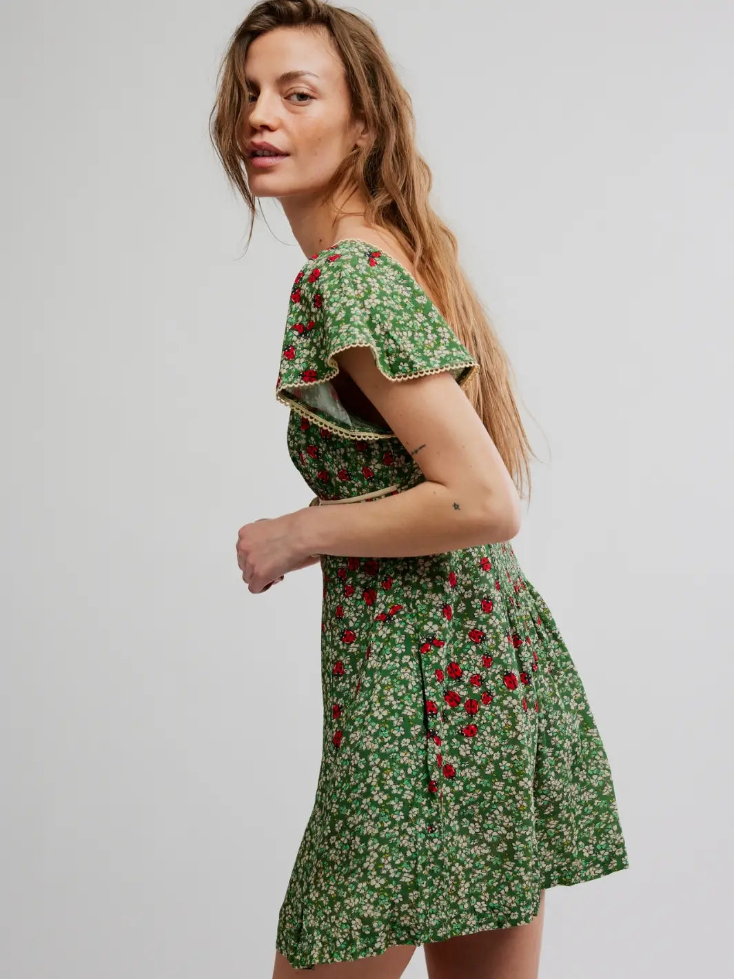 Woman wearing a green 'Backroads Mini in Forest Combo' floral dress from Free People on a white background, side view | Twentyseven Toronto
