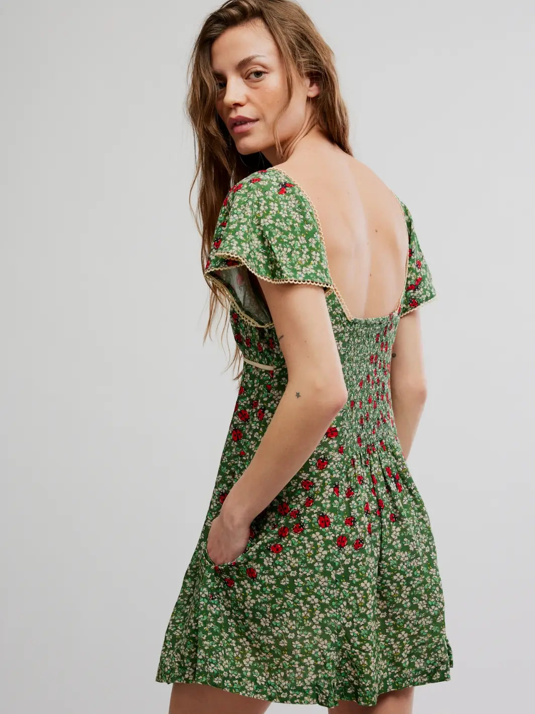 Woman wearing a green 'Backroads Mini in Forest Combo' floral dress from Free People on a white background, back view | Twentyseven Toronto