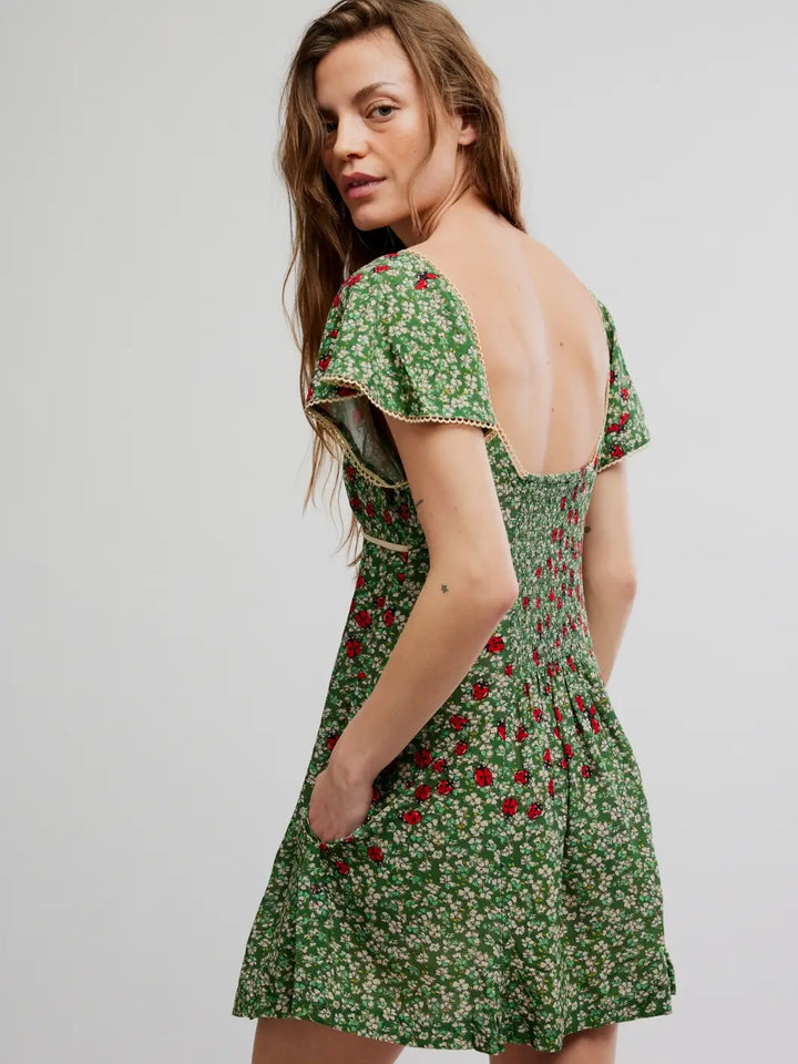 Woman wearing a green 'Backroads Mini in Forest Combo' floral dress from Free People on a white background, back view | Twentyseven Toronto