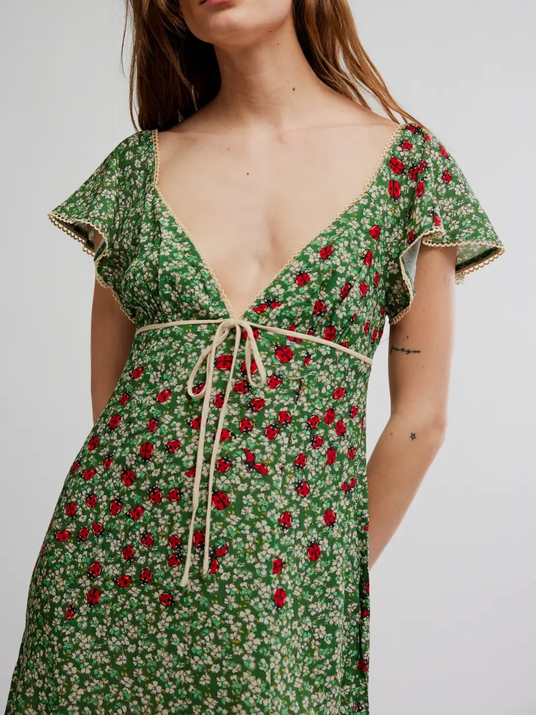 Close up of woman wearing a green 'Backroads Mini in Forest Combo' floral dress from Free People on a white background | Twentyseven Toronto