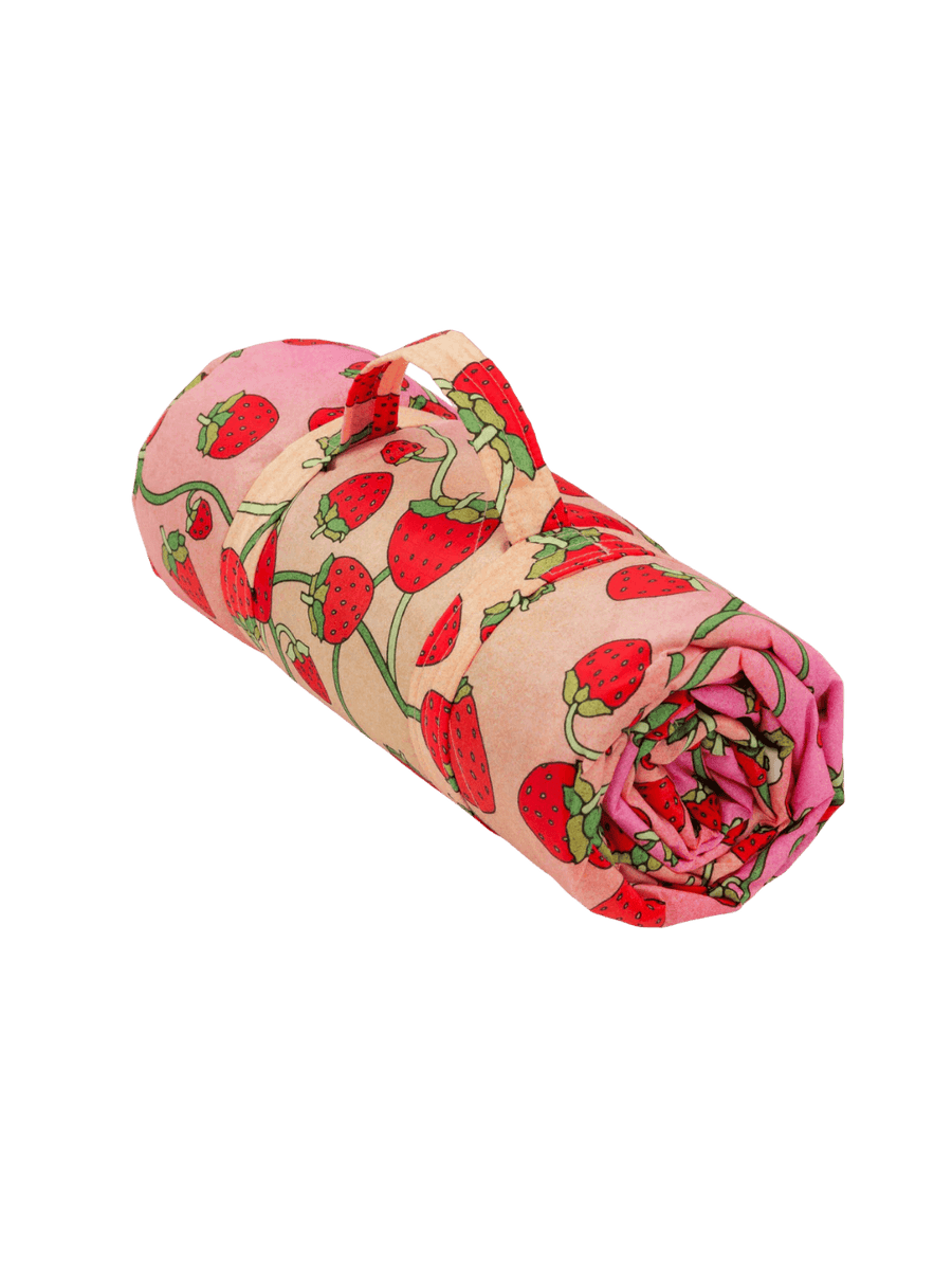 The Baggu Puffy Picnic Blanket in Strawberry Blossom print featuring a pink and peach gradient background layered with an all-over red strawberry and green vine print transparent background | Twentyseven Toronto
