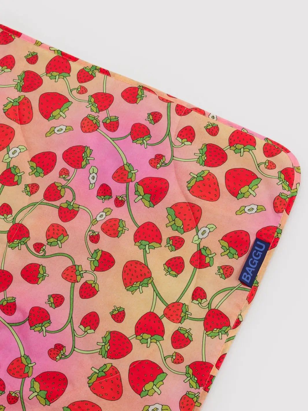 A close-up image of the Baggu Puffy Picnic Blanket - Strawberry Blossom highlighting the quilted nylon texture and an all-over red strawberry and green vine print | Twentyseven Toronto