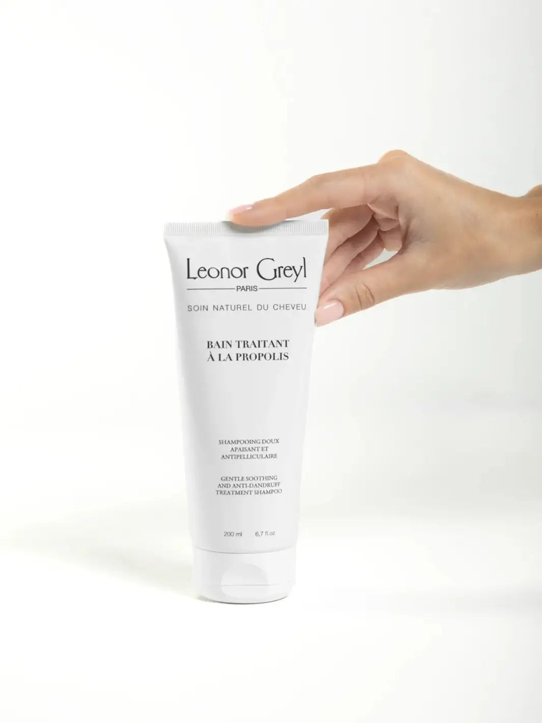 Hand holding a Leonor Greyl 'Bain Traitant à la Propolis' shampoo on a white background | Twentyseven Toronto