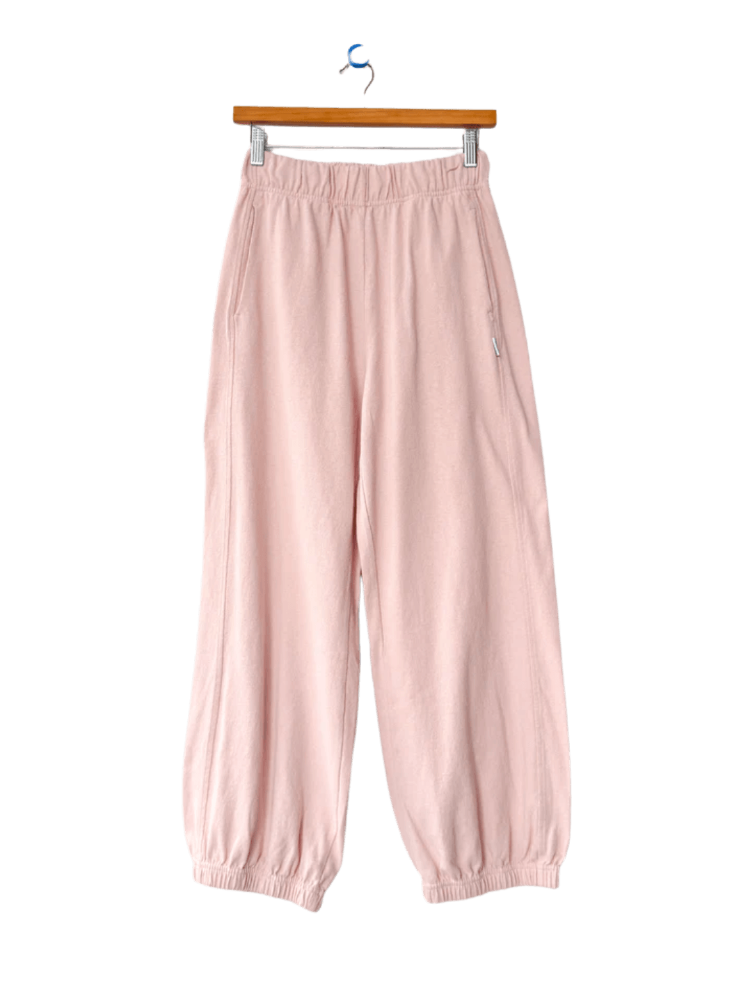 A pair of light pink Le Bon Shoppe Balloon Pants in Baby Pink with a gathered elastic waist and tapered ankle cuffs hangs from a wooden hanger | Twentyseven Toronto