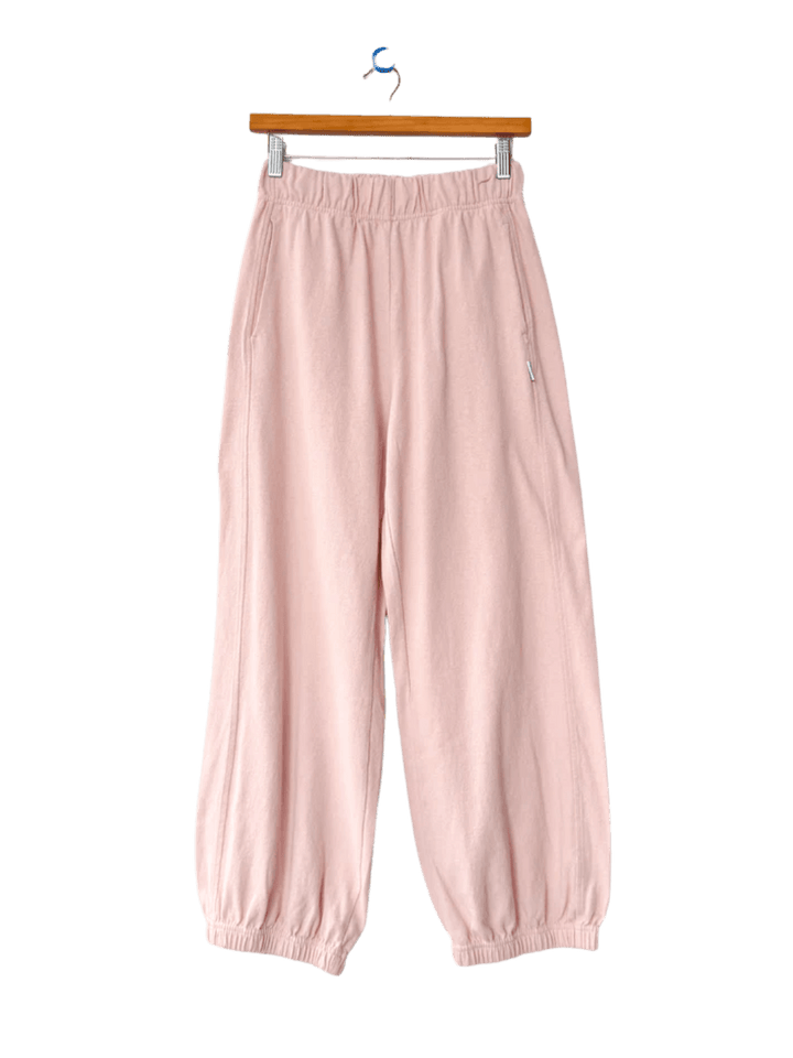 A pair of light pink Le Bon Shoppe Balloon Pants in Baby Pink with a gathered elastic waist and tapered ankle cuffs hangs from a wooden hanger | Twentyseven Toronto