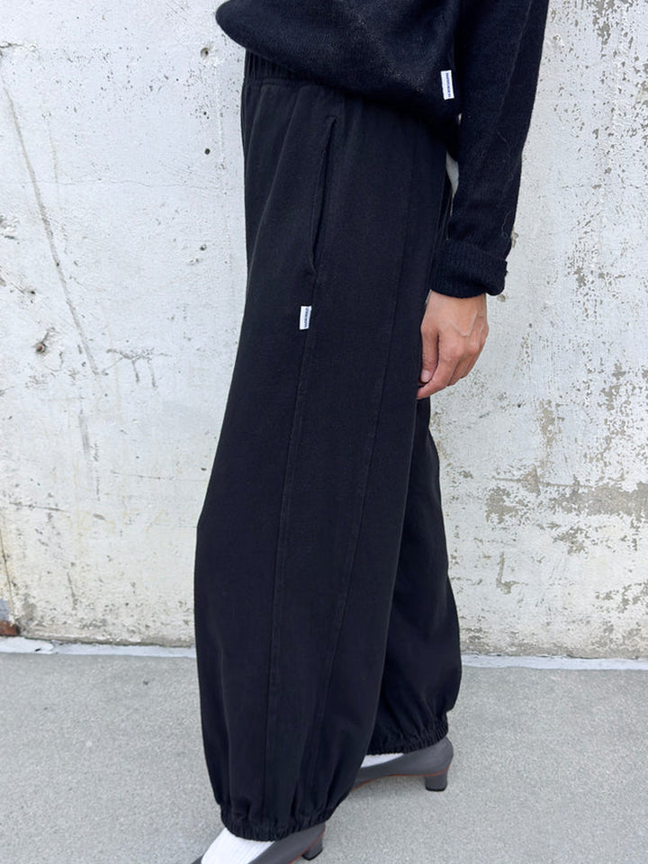 Side view of model wearing black Balloon Pants with a relaxed, voluminous silhouette, side pockets and elasticated cuffs, styled with a black sweater and grey heels | Twentyseven Toronto