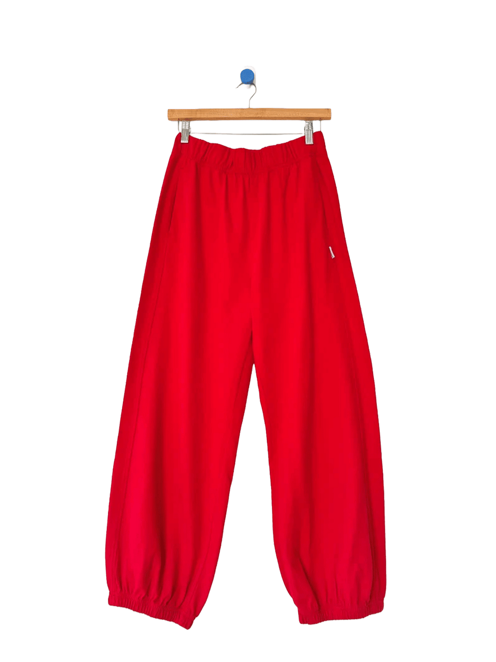Red balloon pants with an elastic waistband and gathered cuffs on a wooden hanger | Twentyseven Toronto