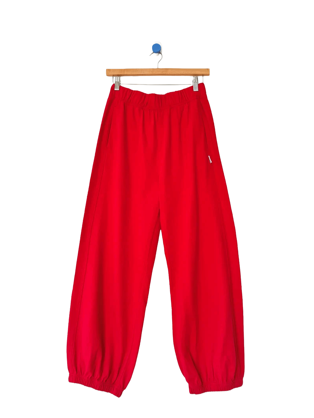 Red balloon pants with an elastic waistband and gathered cuffs on a wooden hanger | Twentyseven Toronto