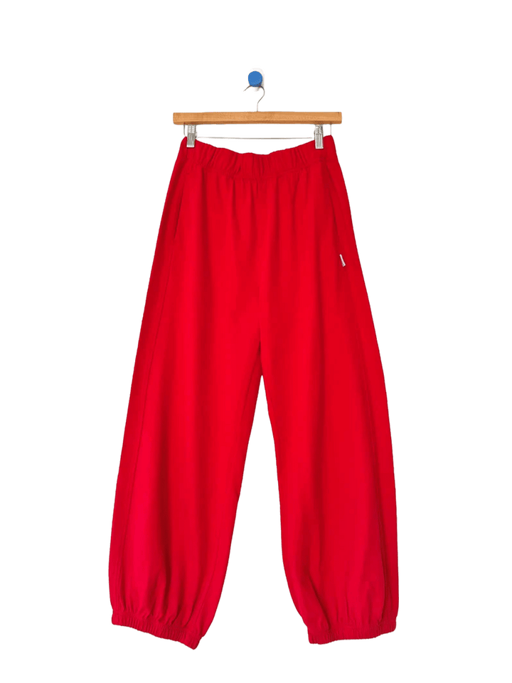 Red balloon pants with an elastic waistband and gathered cuffs on a wooden hanger | Twentyseven Toronto