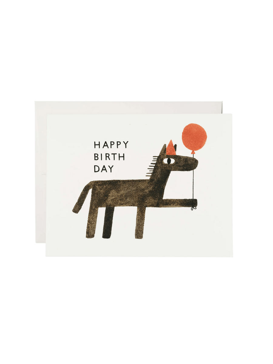 A Balloon Wishes Greeting Card from Red Cap Cards features a minimalist illustration of a dark brown horse wearing a red party hat and holding a red balloon next to the text "HAPPY BIRTH DAY," pictured with a white envelope | Twentyseven Toronto