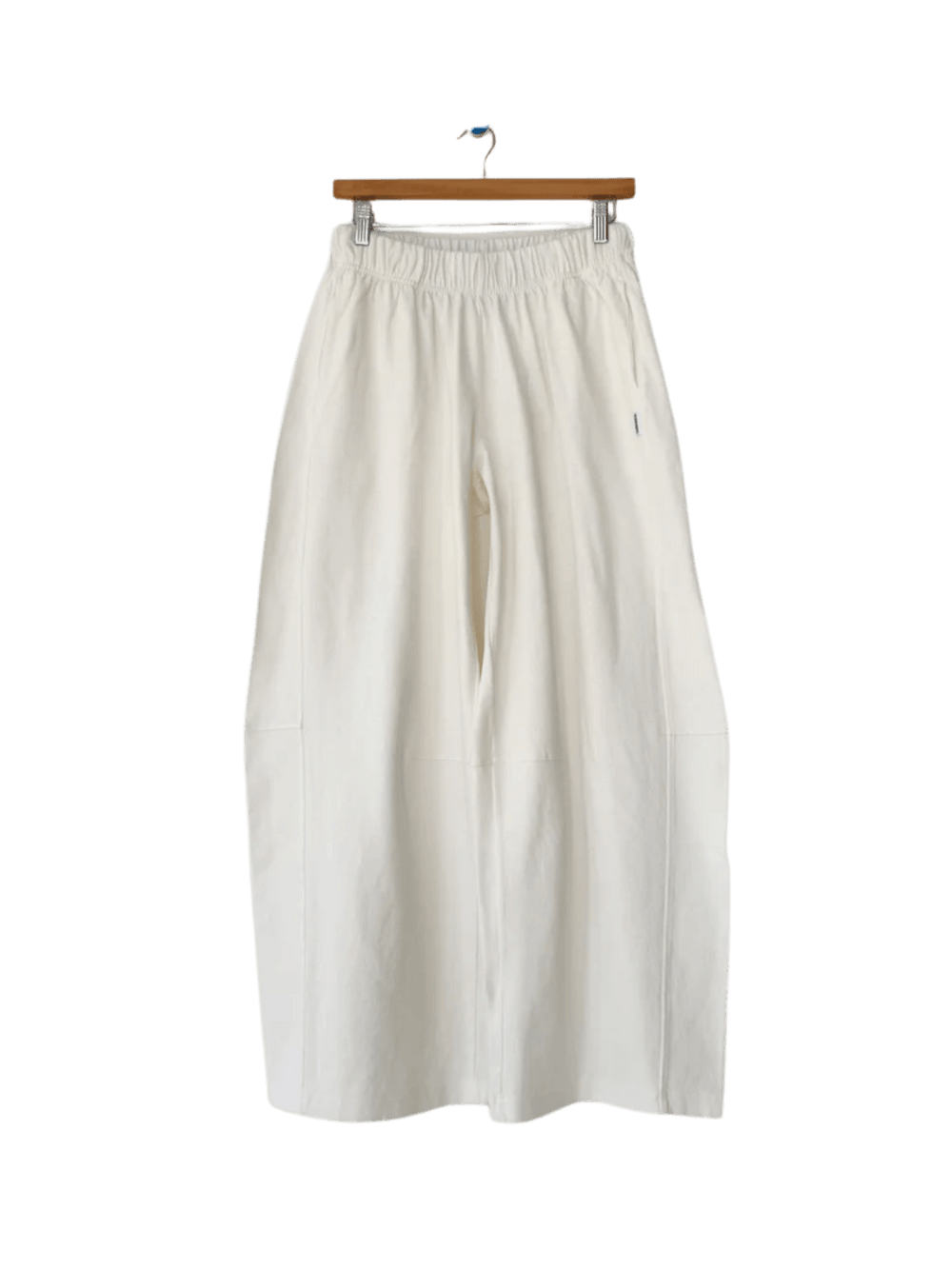 The wide-leg Le Bon Shoppe Bare Pants in White Cotton hang vertically from a wooden skirt hanger with metal clips | Twentyseven Toronto