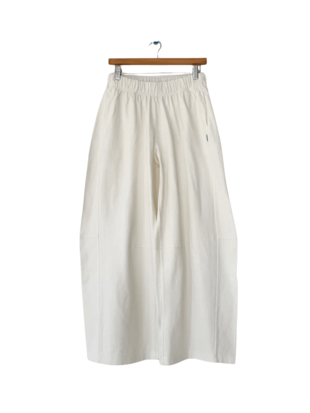 The wide-leg Le Bon Shoppe Bare Pants in White Cotton hang vertically from a wooden skirt hanger with metal clips | Twentyseven Toronto