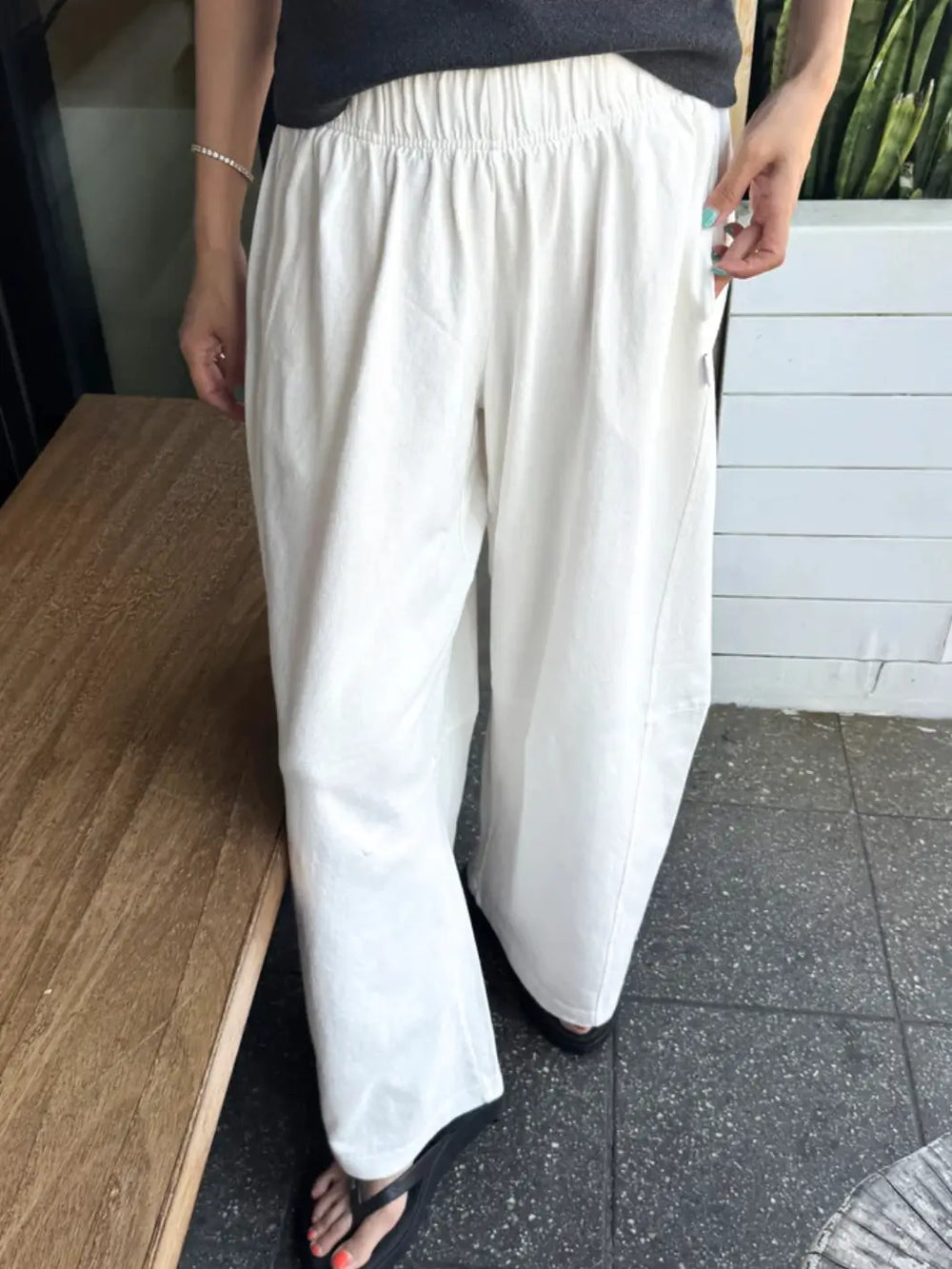 A model wears the loose, comfortable Le Bon Shoppe Bare Pants in White Cotton featuring a gathered elastic waistband and side pockets, paired with black flip-flops | Twentyseven Toronto