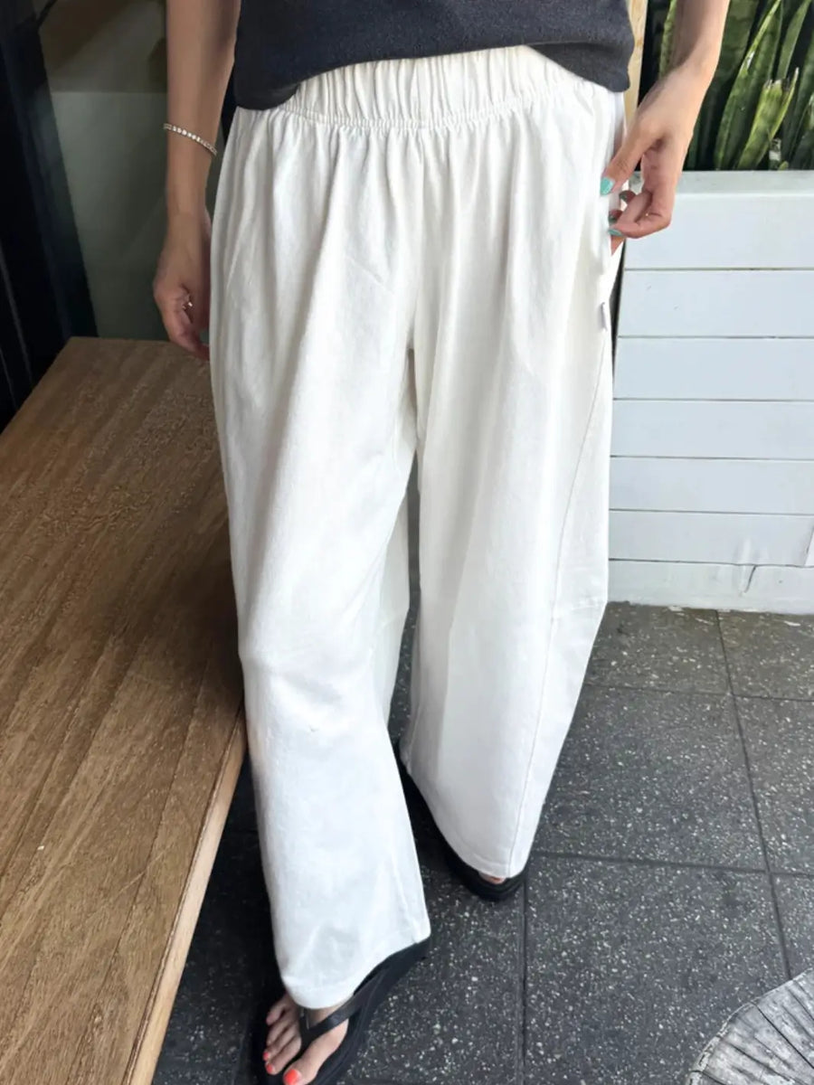 A model wears the loose, comfortable Le Bon Shoppe Bare Pants in White Cotton featuring a gathered elastic waistband and side pockets, paired with black flip-flops | Twentyseven Toronto
