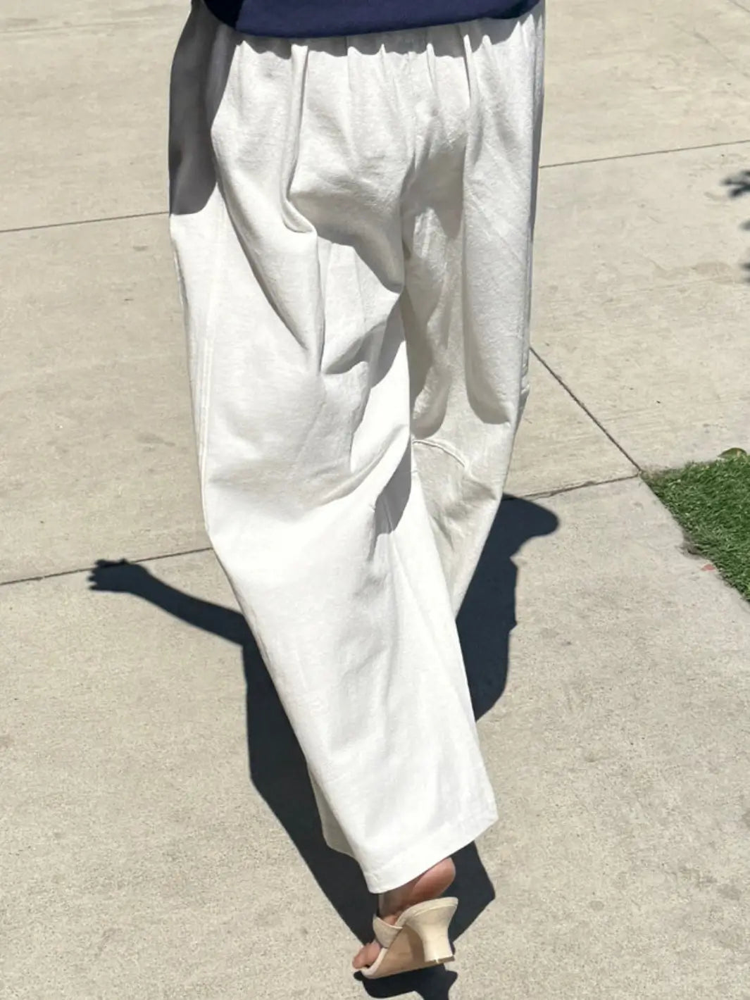 A model walks down a sunny sidewalk wearing the Le Bon Shoppe Bare Pants in White Cotton, showcasing the flowy, wide-leg fit from behind | Twentyseven Toronto