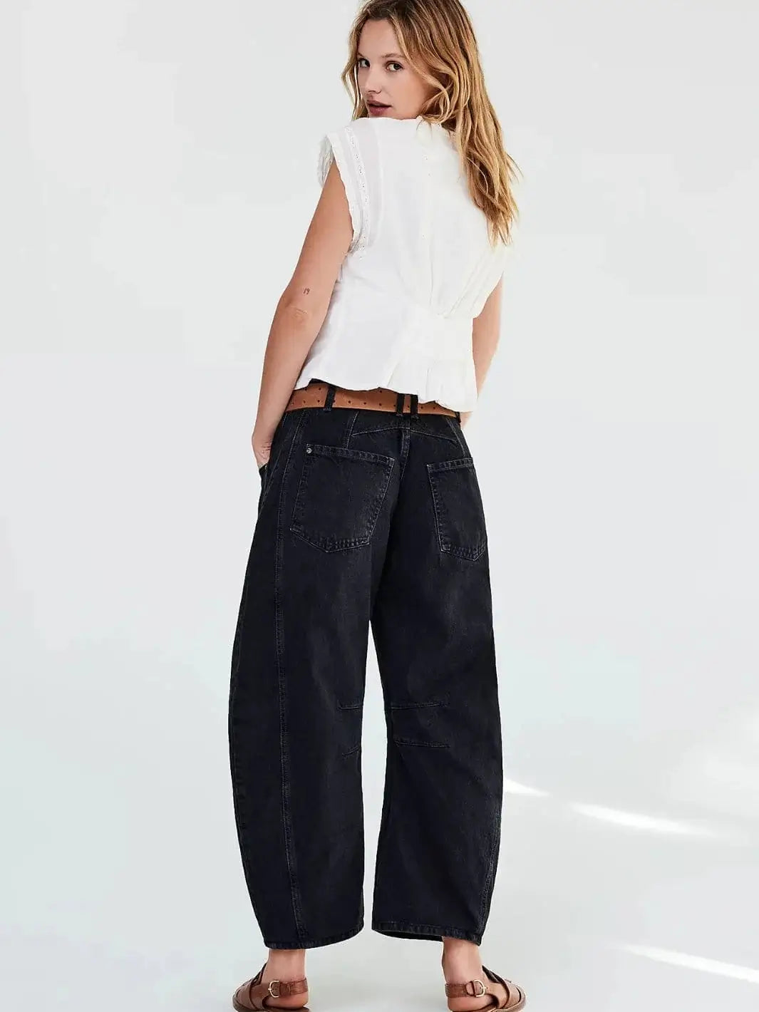 A view from behind shows a model wearing the Free People Good Luck Mid-Rise Barrel Jeans - Soundwave paired with a white sleeveless top and brown leather sandals | Twentyseven Toronto