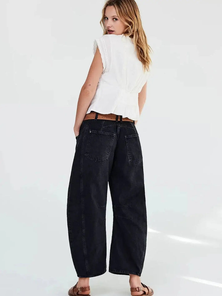 A view from behind shows a model wearing the Free People Good Luck Mid-Rise Barrel Jeans - Soundwave paired with a white sleeveless top and brown leather sandals | Twentyseven Toronto