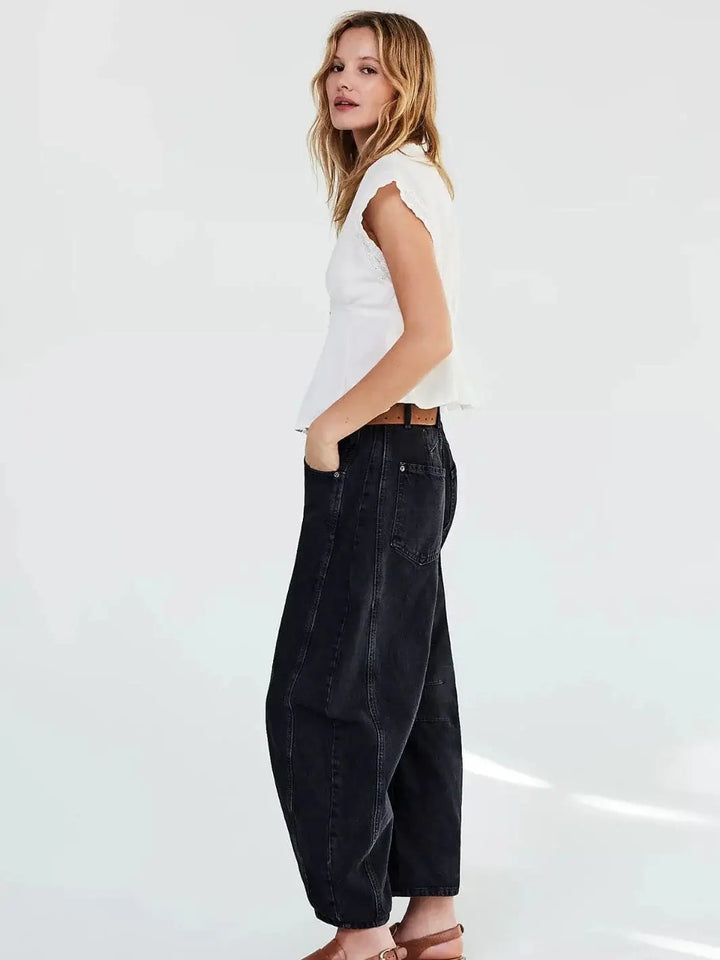 A side-profile view of a model standing against a white backdrop in the wide-leg Free People Good Luck Mid-Rise Barrel Jeans - Soundwave and a white top | Twentyseven Toronto