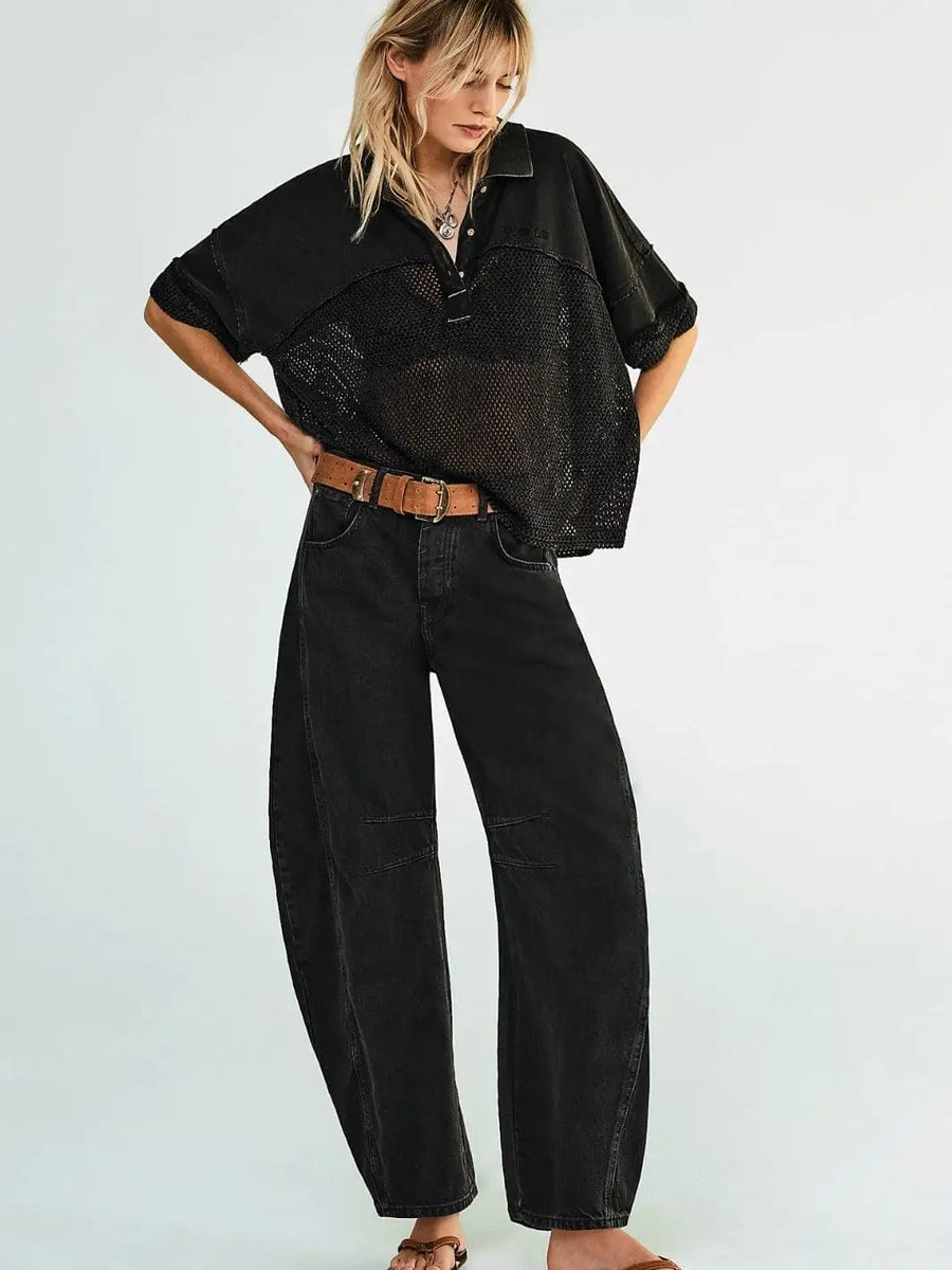 A model poses looking down while wearing the slouchy Free People Good Luck Mid-Rise Barrel Jeans - Soundwave with a brown belt and an oversized black mesh polo shirt | Twentyseven Toronto