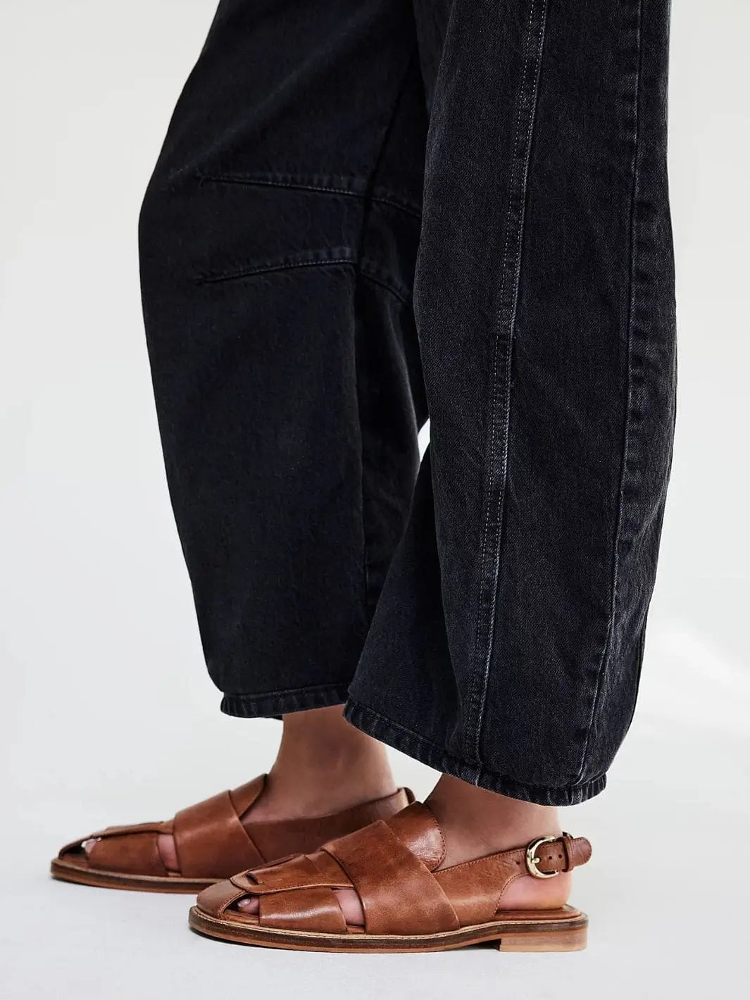 A close-up shot focuses on the cropped cuffs and curved side seams of the Free People Good Luck Mid-Rise Barrel Jeans - Soundwave worn with brown leather fisherman sandals | Twentyseven Toronto