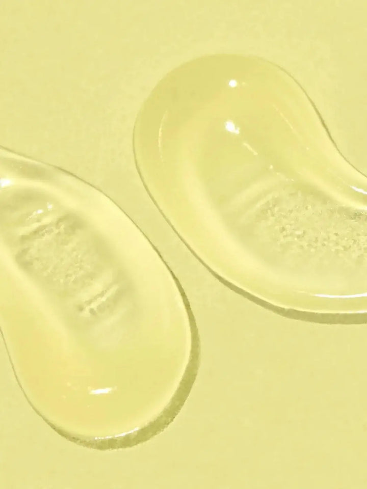 A close-up view displays two clear, smooth dollops of gel on a solid yellow surface, highlighting the clear texture of Bask Suncare Daily Invisible Gel SPF 40 Sunscreen | Twentyseven Toronto