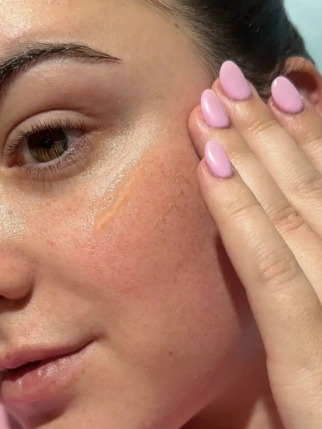 A close-up shows a person with pink manicured nails applying a smooth layer of Bask Suncare Daily Invisible Gel SPF 40 Sunscreen on their cheek | Twentyseven Toronto