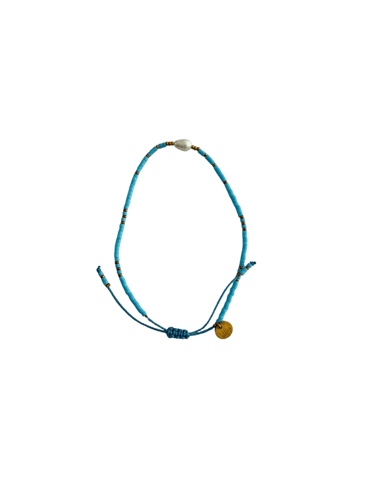Bracelet with blue cord, small blue and gold beads and single white pearl with gold charm on a transparent background | Twentyseven Toronto