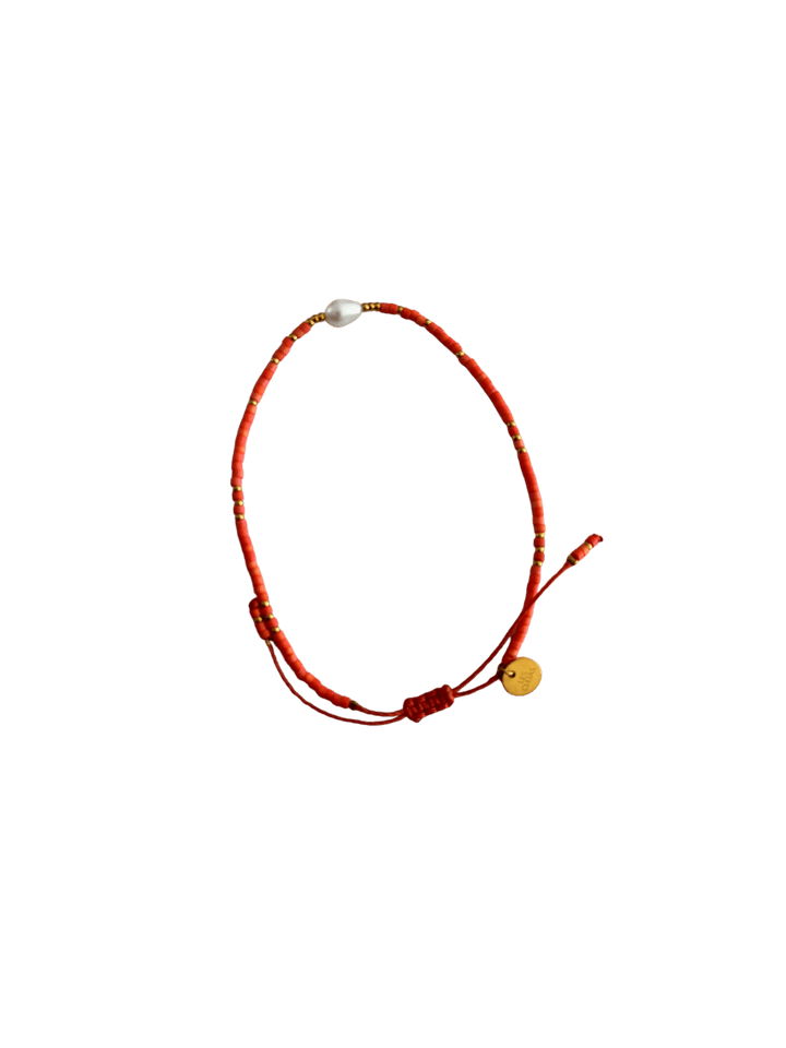 Bracelet with red cord, small red and gold beads and single white pearl with gold charm on a transparent background | Twentyseven Toronto