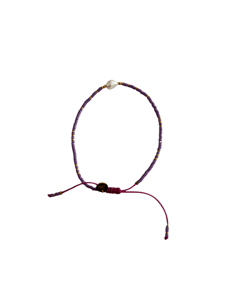 Bracelet with purple cord, small purple and gold beads and single white pearl with gold charm on a transparent background | Twentyseven Toronto