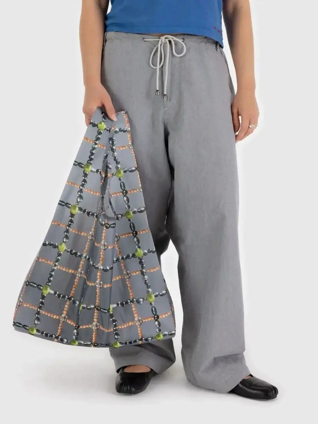 A close-up shot shows a person holding the gray Baggu Beaded Plaid Bag by its handle, highlighting the detailed print of intersecting strands of pearls and beads | Twentyseven Toronto