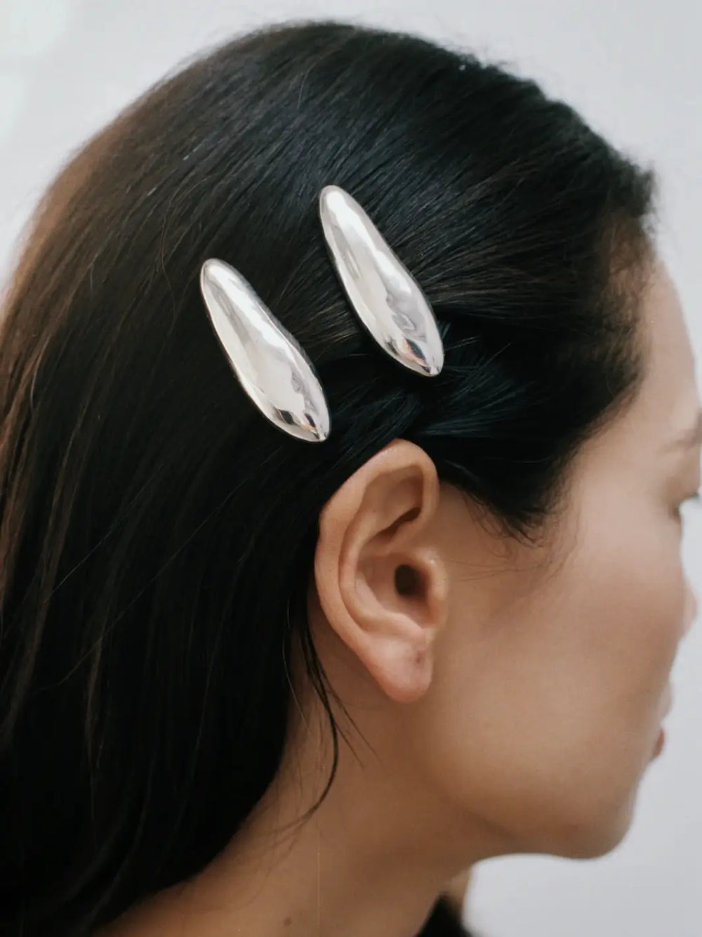 A side view of a person with dark hair wearing two shiny, liquid-metal Bean Clips in Silver from Wolf Circus pinned closely together above the ear | Twentyseven Toronto