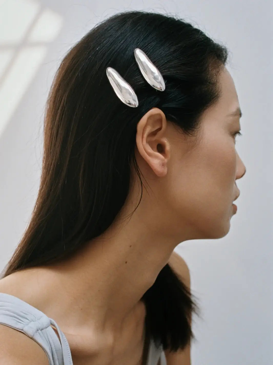A side shot of a model showcasing the modern, reflective design of two Bean Clips in Silver from Wolf Circus styled in her dark hair | Twentyseven Toronto