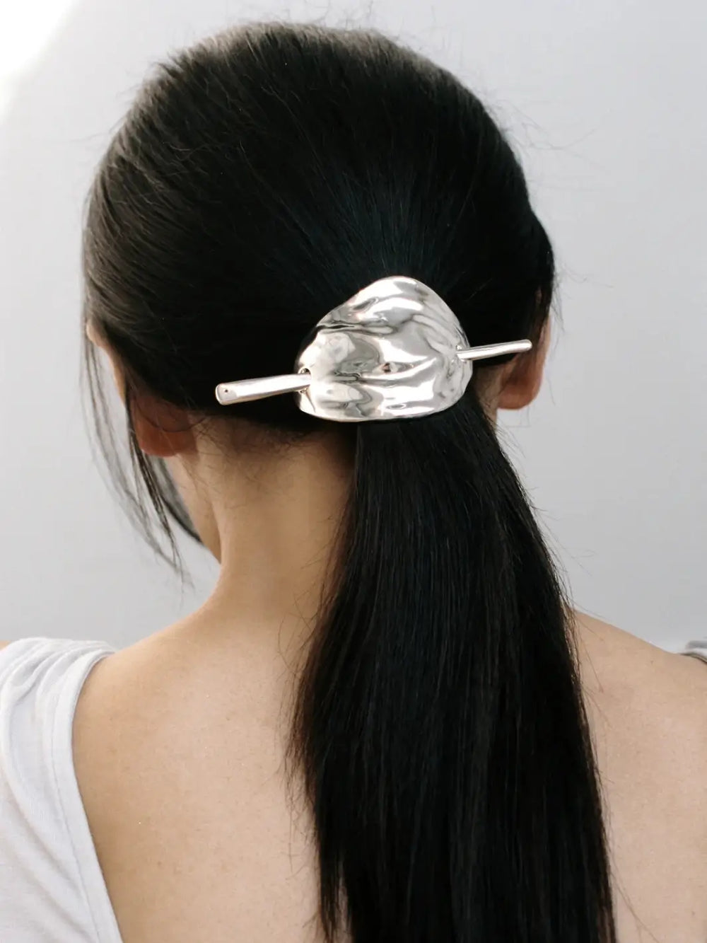 A woman's dark hair styled in a low ponytail, secured with the silver molten-textured Bean French Pin in Silver from Wolf Circus | Twentyseven Toronto