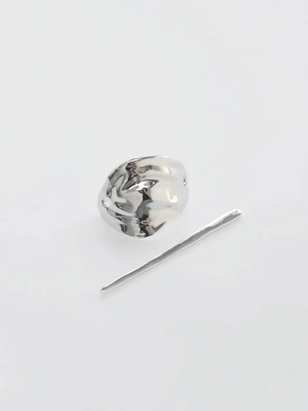 The two separate components of the Bean French Pin in Silver from Wolf Circus, including the curved metallic shield and the straight fastening stick on a white background | Twentyseven Toronto