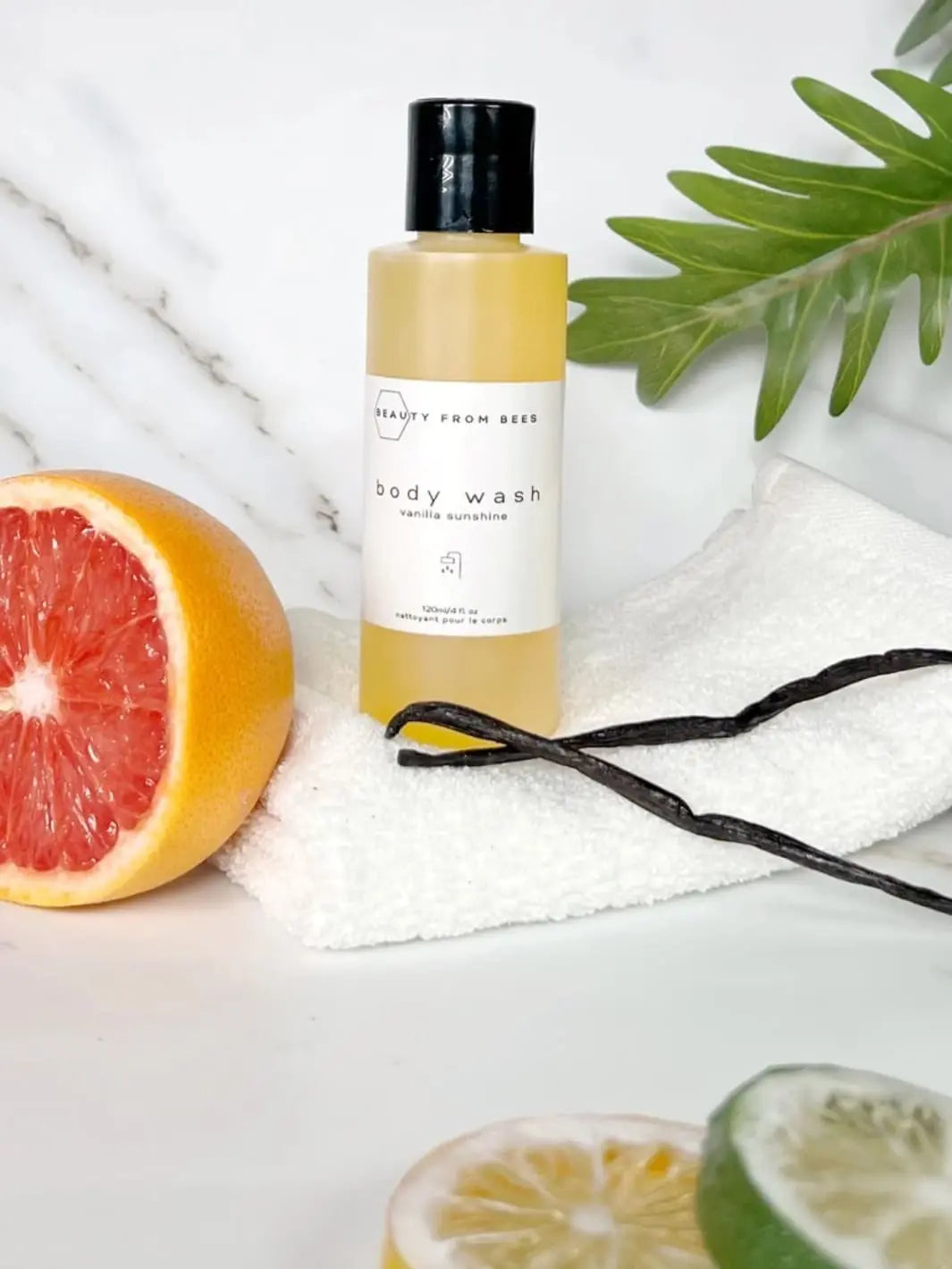 Beauty from Bees Body Wash | Twentyseven Toronto | Beauty from Bees Body Wash bottle with a half-grapefruit, vanilla bean, and lime on a white background