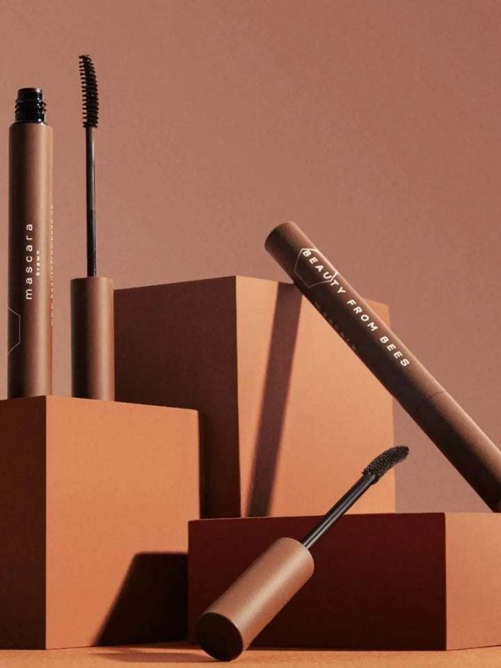 Studio display featuring tubes and wands of Beauty from Bees Mascara in Black arranged on warm brown geometric pedestals | Twentyseven