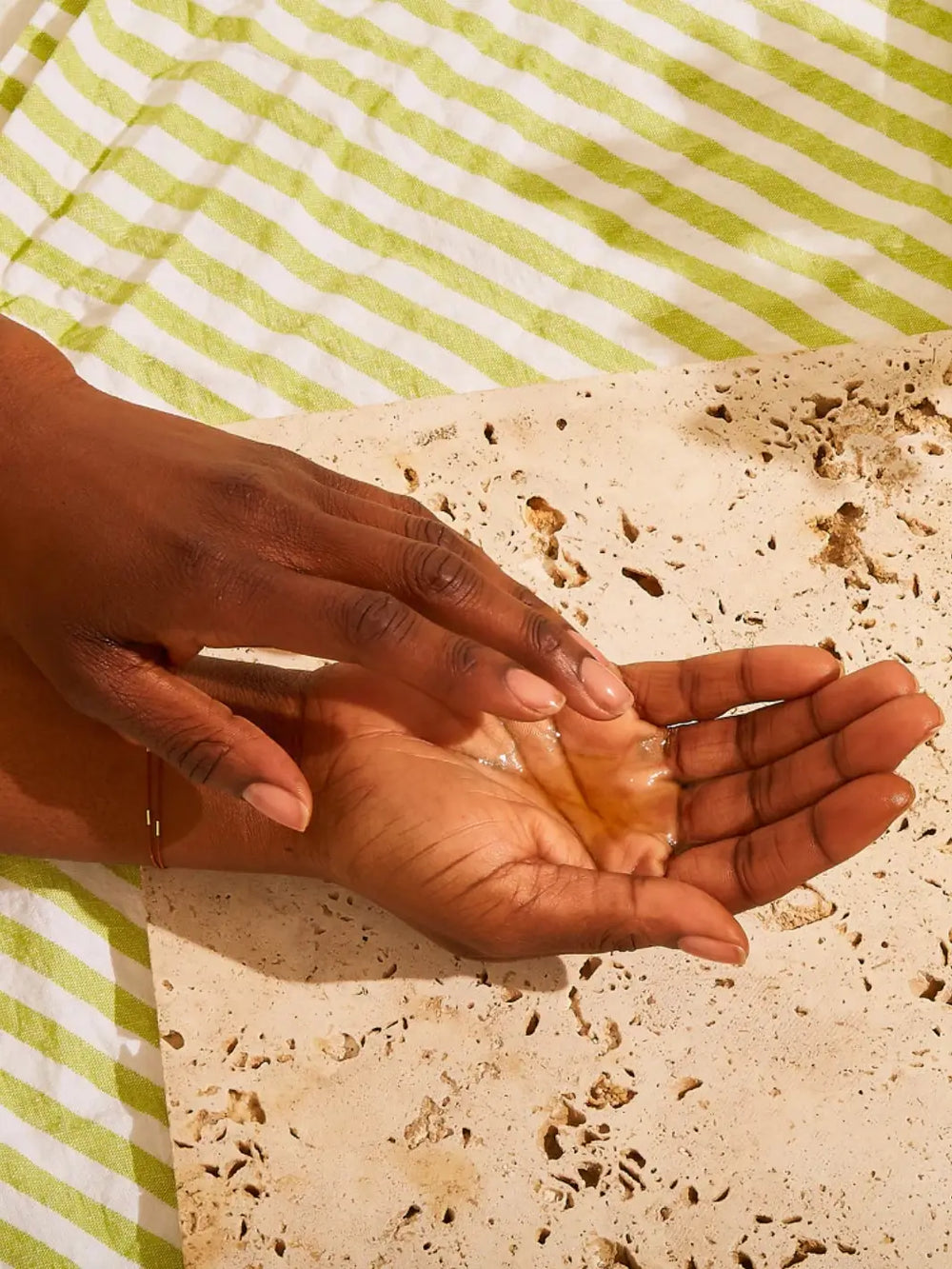 Hands using Olio E Osso Bel Corpo Body Oil on a yellow background | Twentyseven Toronto
