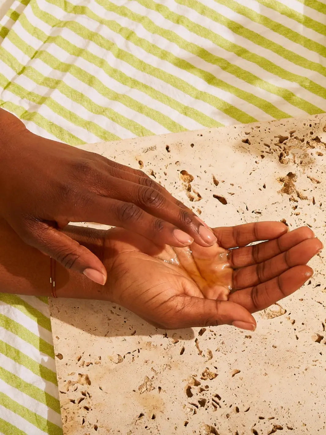 Hands using Olio E Osso Bel Corpo Body Oil on a yellow background | Twentyseven Toronto