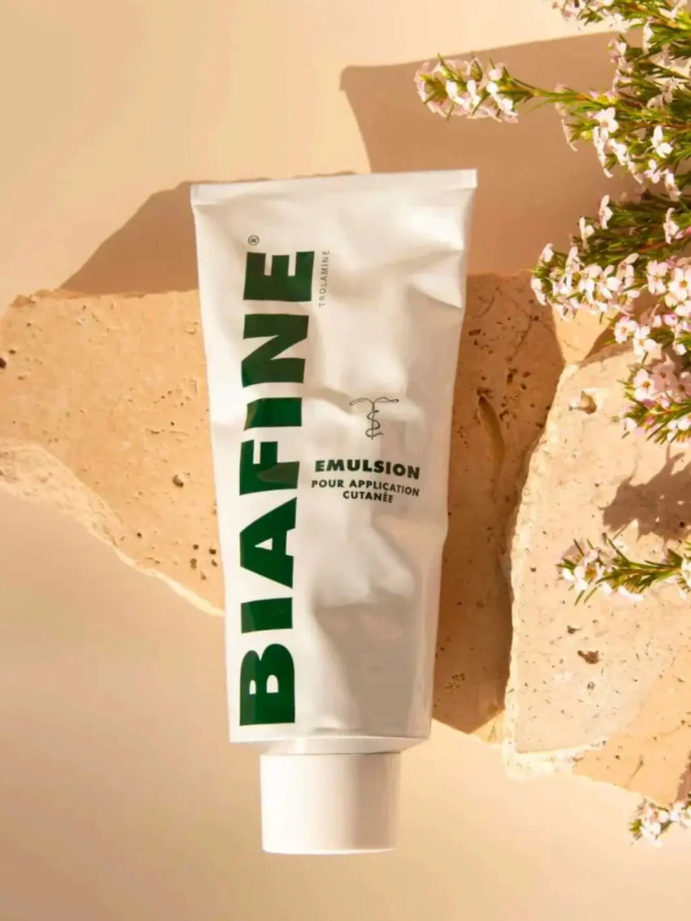 A white tube of Biafine Emulsion Cream on a textured beige stone surrounded by small pink and white wildflowers | Twentyseven Toronto