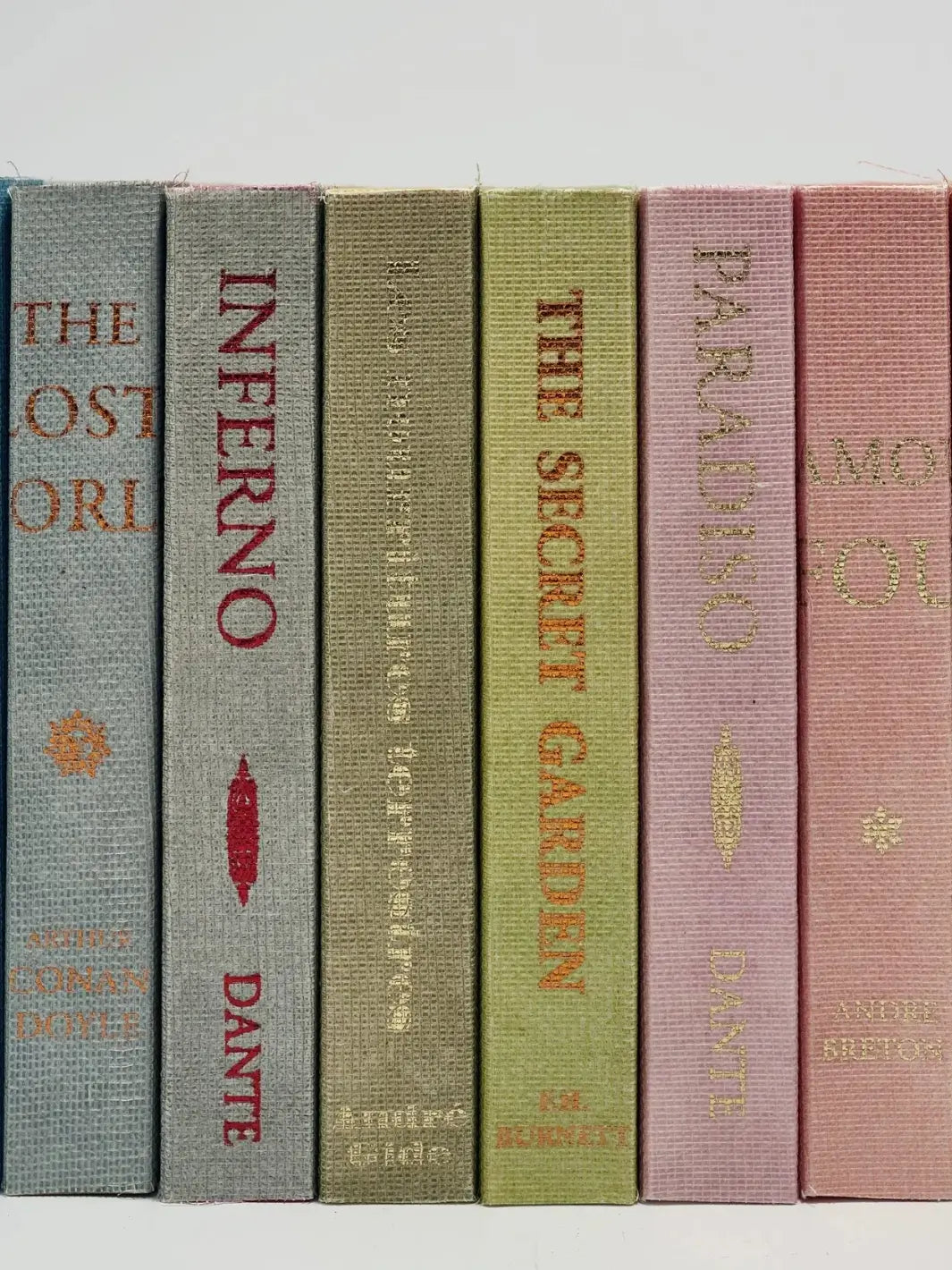 A close-up view showing the textured cloth spines of six notebooks aligned vertically, displaying classic titles like Inferno and The Secret Garden from the Biblioteca Muta Slow Design collection | Twentyseven Toronto