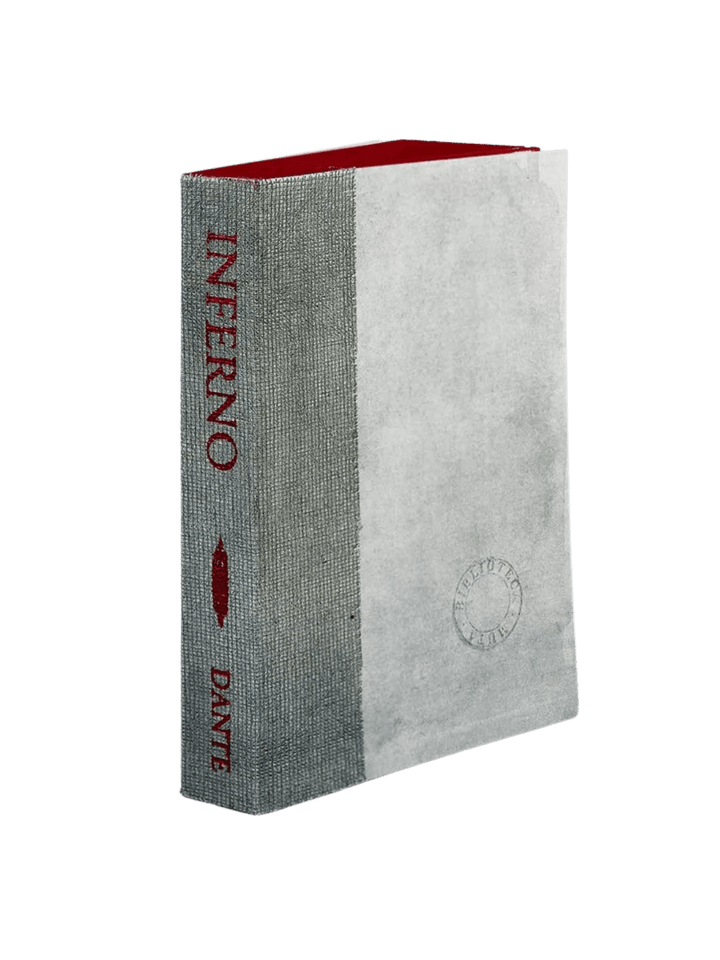 A notebook of Inferno from the Slow Design Biblioteca Muta collection features a textured grey gauze spine stamped with deep red literary typography alongside a pale parchment-style cover bearing a circular library seal | Twentyseven Toronto