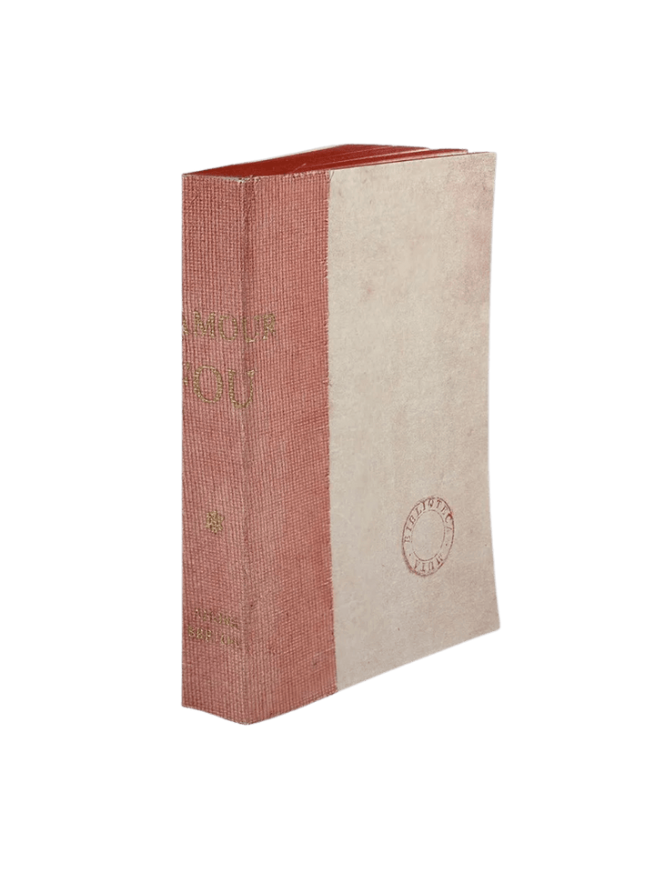 A notebook L'Amour Fou from the Slow Design Biblioteca Muta collection features a textured pink gauze spine stamped with gold literary typography alongside a pale, parchment-style cover bearing a circular library seal | Twentyseven Toronto