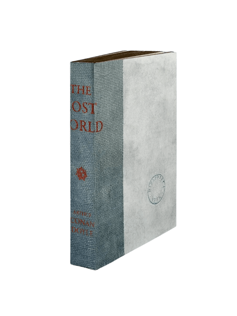 A notebook from the The Lost World from Slow Design Biblioteca Muta collection features a textured gray gauze spine stamped with orange literary typography alongside a parchment-style cover bearing a circular library seal | Twentyseven Toronto