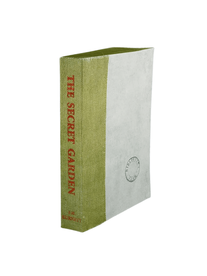 A Biblioteca Muta: The Secret Garden journal from Slow Design featuring a light green gauze spine stamped with a red literary title alongside a textured, parchment-like cover bearing a circular library seal | Twentyseven Toronto